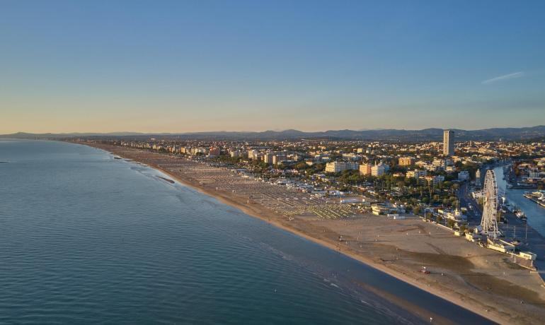 Sunset beach, calm sea, vibrant city on the horizon.