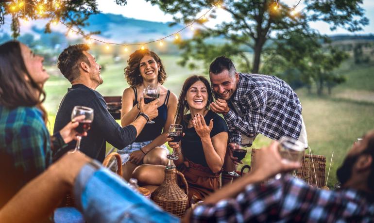 Amici che si divertono all'aperto con vino e luci decorative.