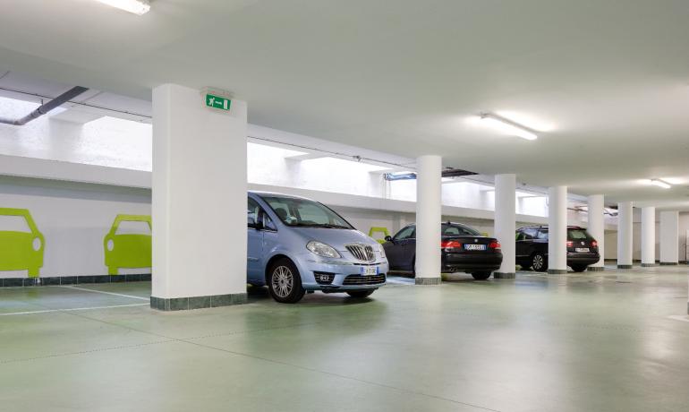 Underground parking with cars and green signage.