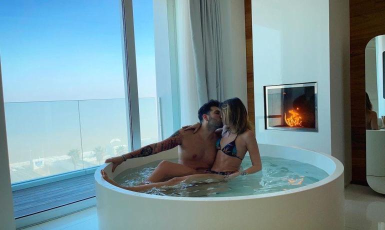 Couple dans un jacuzzi avec vue sur la mer et cheminée allumée.
