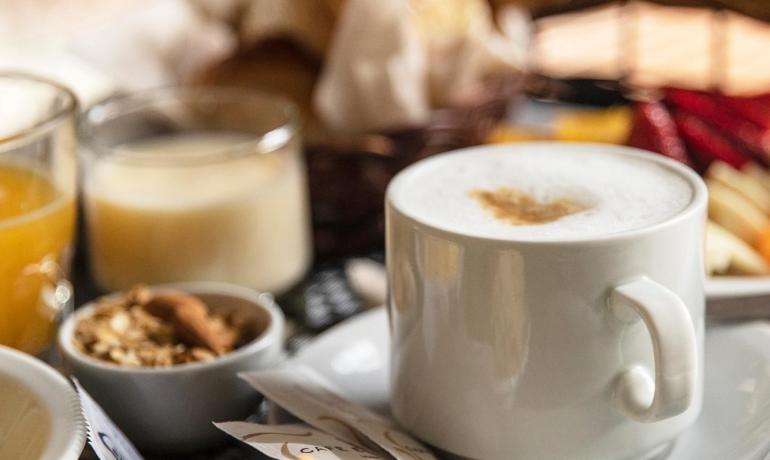Breakfast with cappuccino, juice, pastries, and cereals in a basket.