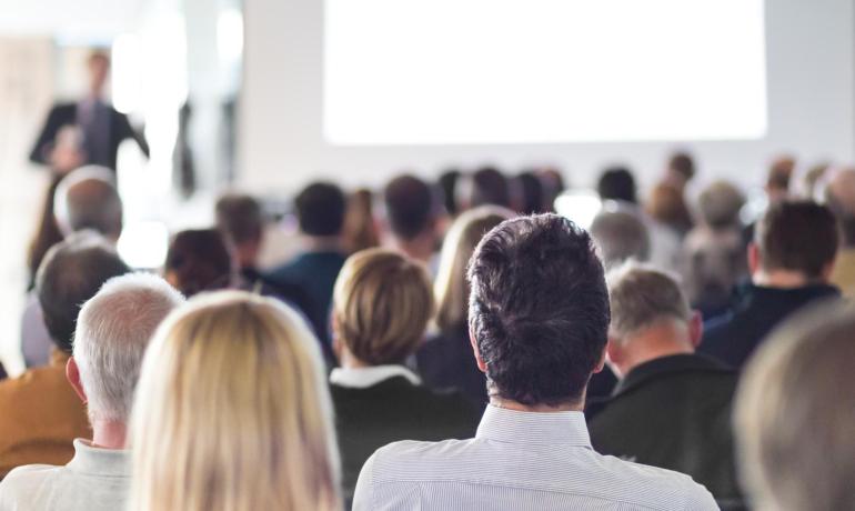 Personnes assises écoutant une présentation dans une salle de conférence.