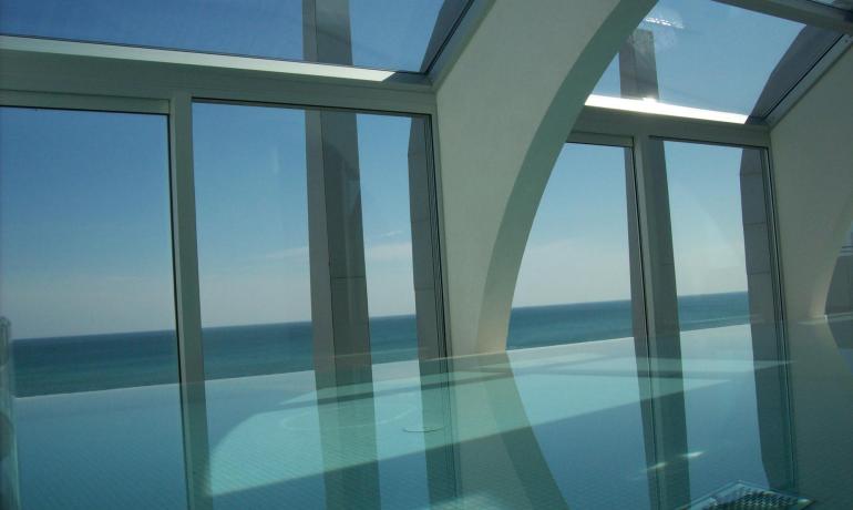 Piscine intérieure avec vue sur la mer, grandes fenêtres et arches blanches.