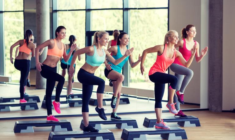 Gruppe von Frauen macht Step-Aerobic in einem hellen Fitnessstudio.