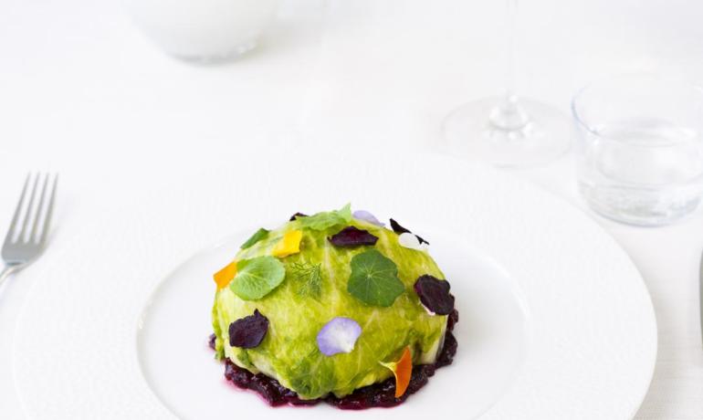 Piatto gourmet con foglie e fiori, accompagnato da vino bianco.