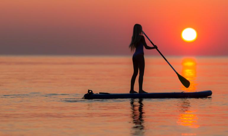 Atemberaubender Sonnenuntergang, Person beim Paddeln, ruhiges und friedliches Meer.