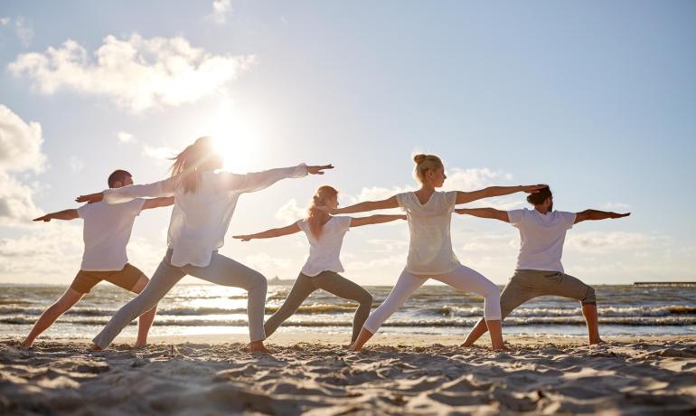 Menschen machen Yoga am Strand bei Sonnenuntergang, ruhige und entspannende Atmosphäre.