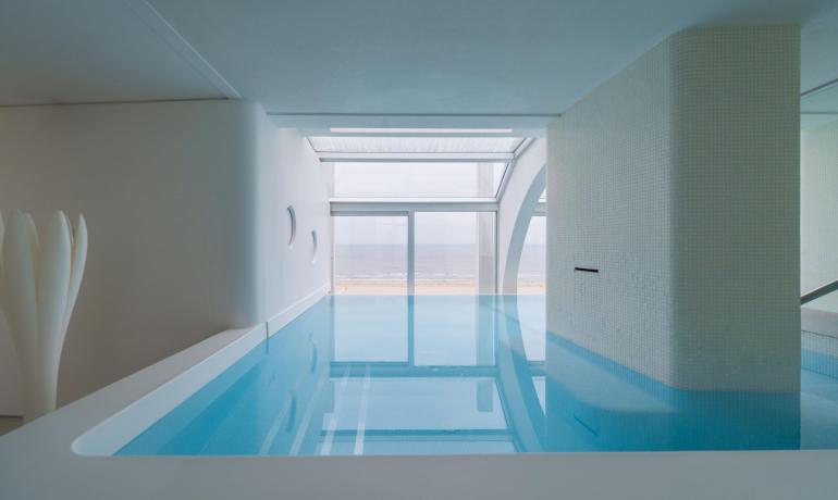 Piscina interna con vista mare attraverso grandi finestre.