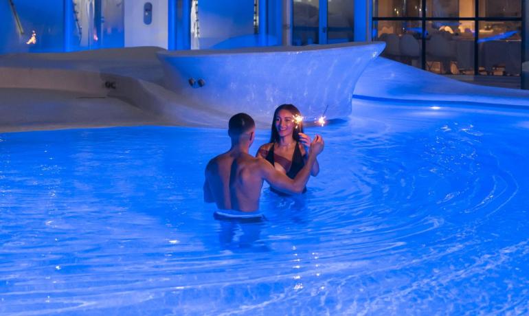Romantic couple in blue-lit pool, magical evening.
