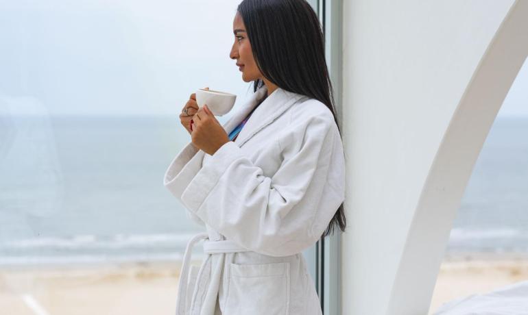 Donna in accappatoio bianco beve caffè con vista mare.