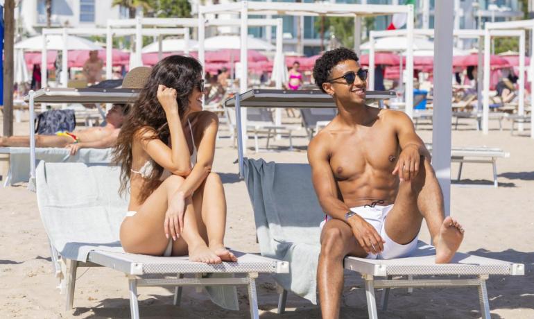 Coppia felice prende il sole su lettini in spiaggia, atmosfera estiva e rilassata.
