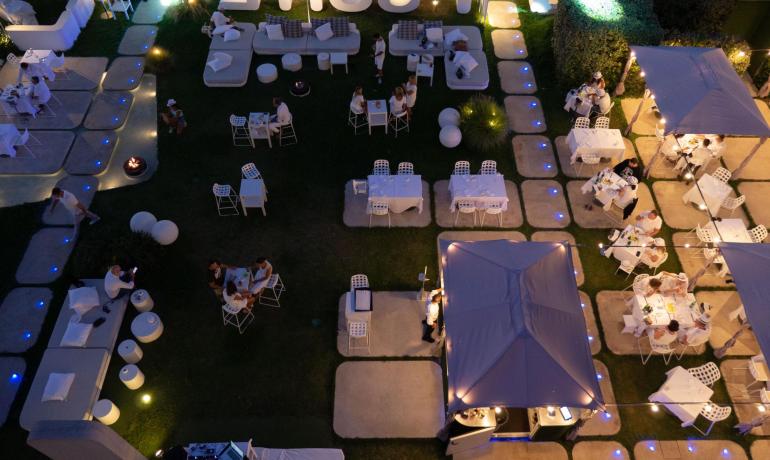 Aerial view of an elegant outdoor evening with soft lights and white tables.