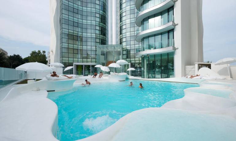 Piscine moderne avec des gens détendus, bâtiment en verre en arrière-plan.