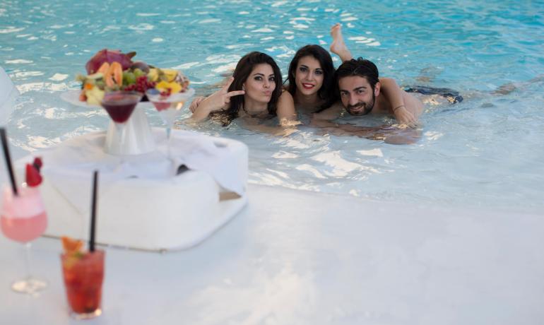 Trois personnes joyeuses dans une piscine avec cocktails et fruits.