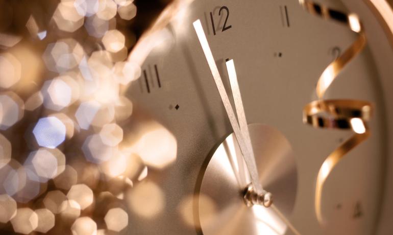 Orologio che segna mezzanotte con luci scintillanti sullo sfondo.