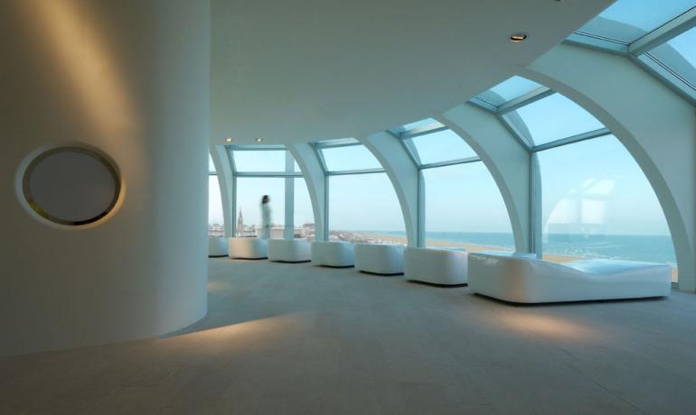 Moderner Raum mit Meerblick, großen Fenstern und weißen Sitzgelegenheiten.