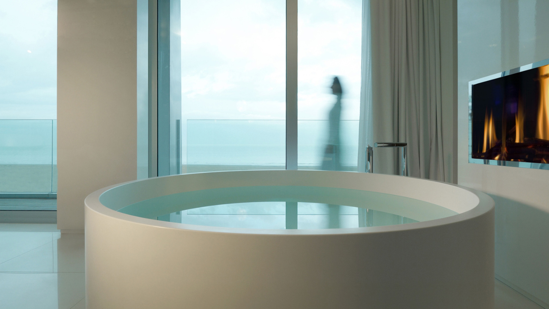 Vasca rotonda in bagno moderno con vista mare e camino acceso.