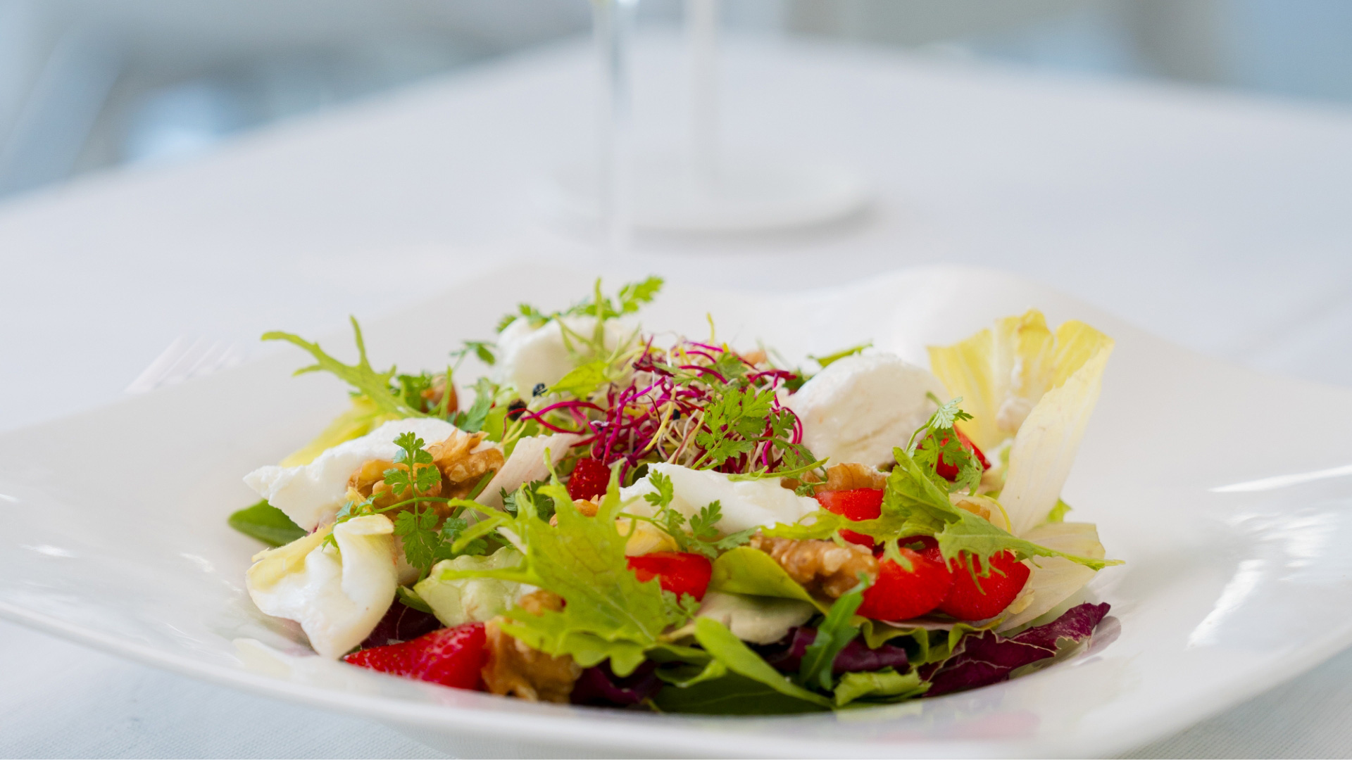 Insalata fresca con noci, formaggio, fragole e verdure miste su piatto bianco.
