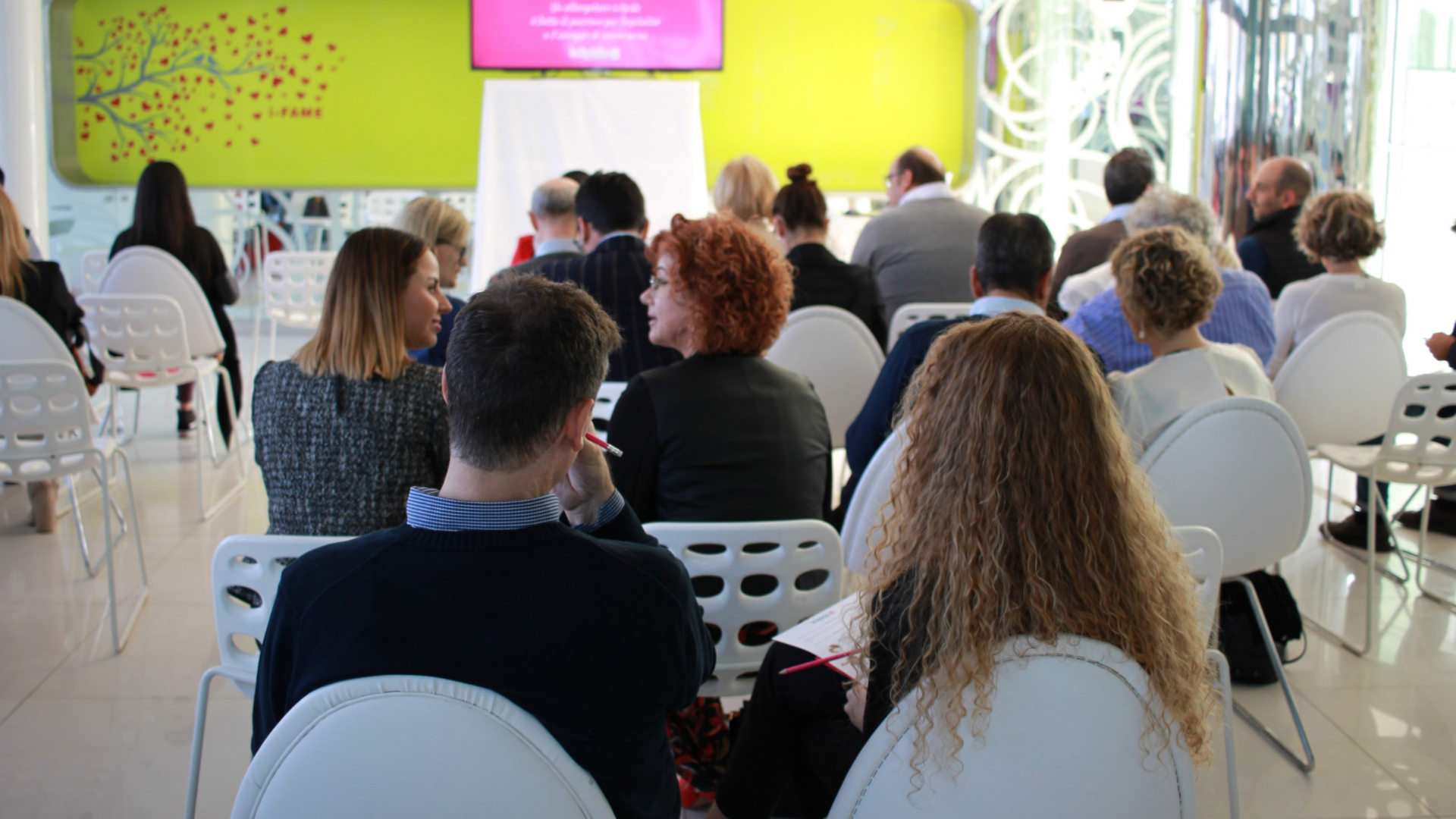 Persone sedute in una sala conferenze, conversando e prendendo appunti.
