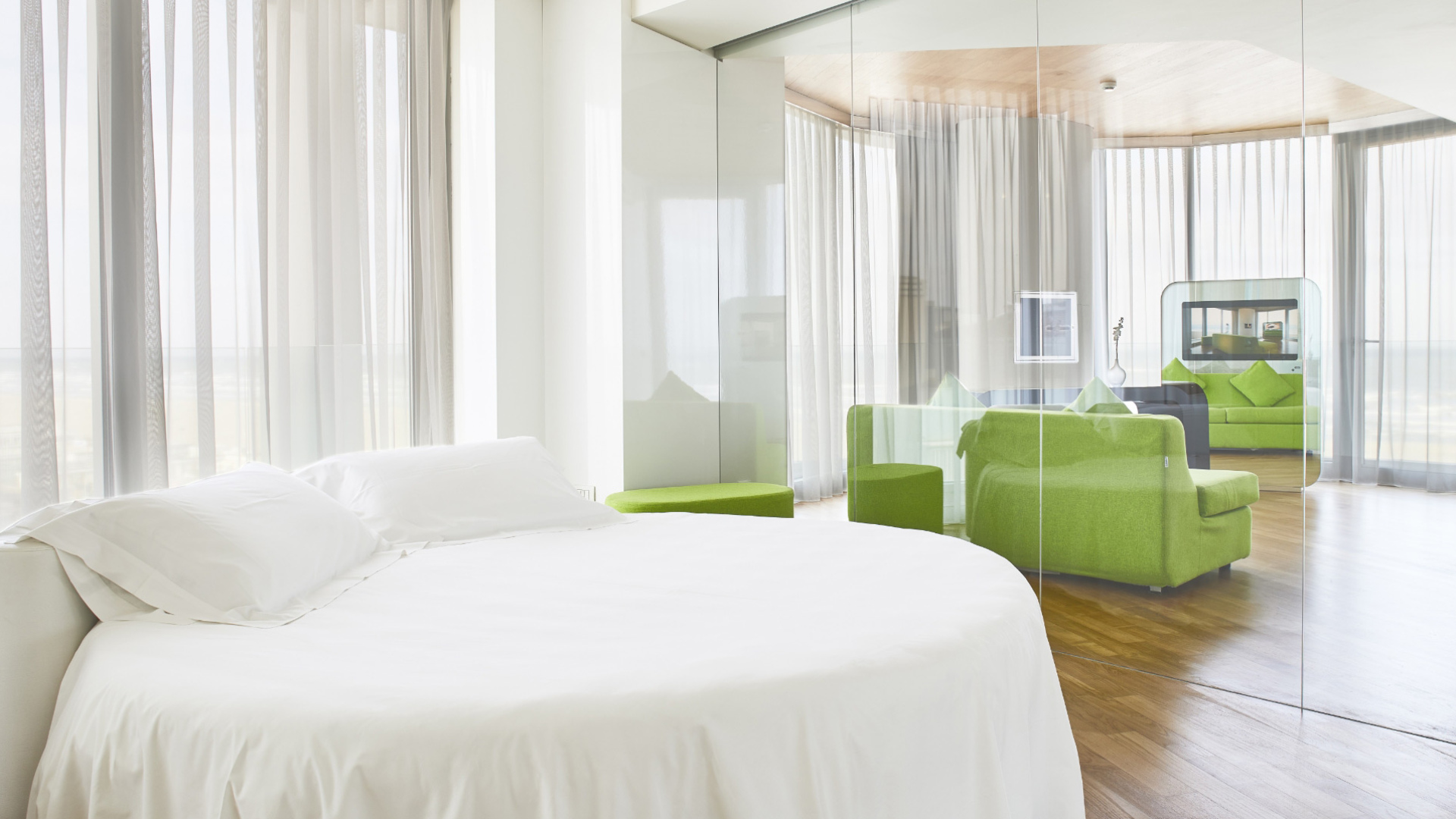 Camera moderna con letto bianco, divano verde e pareti di vetro.