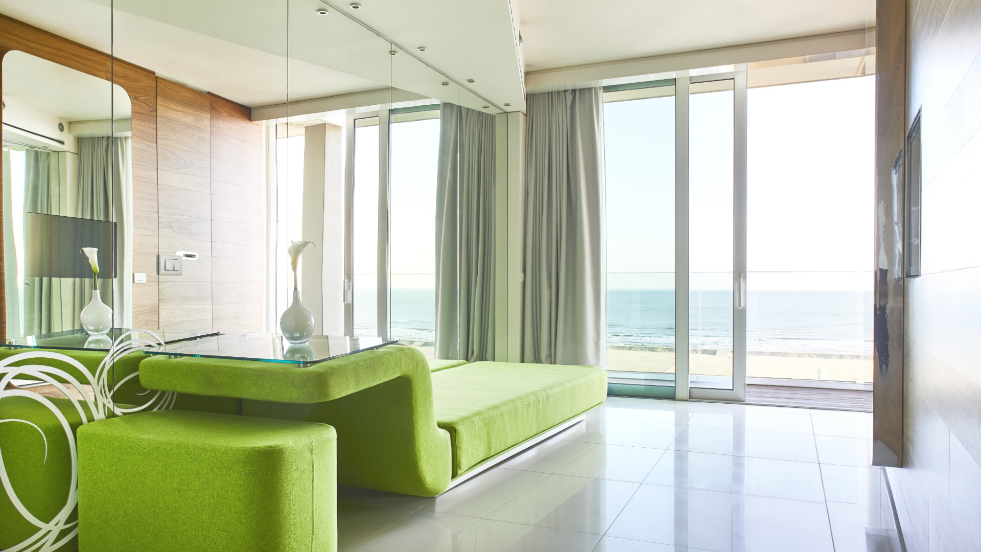 Salotto moderno con vista mare, arredi verdi e ampie vetrate.