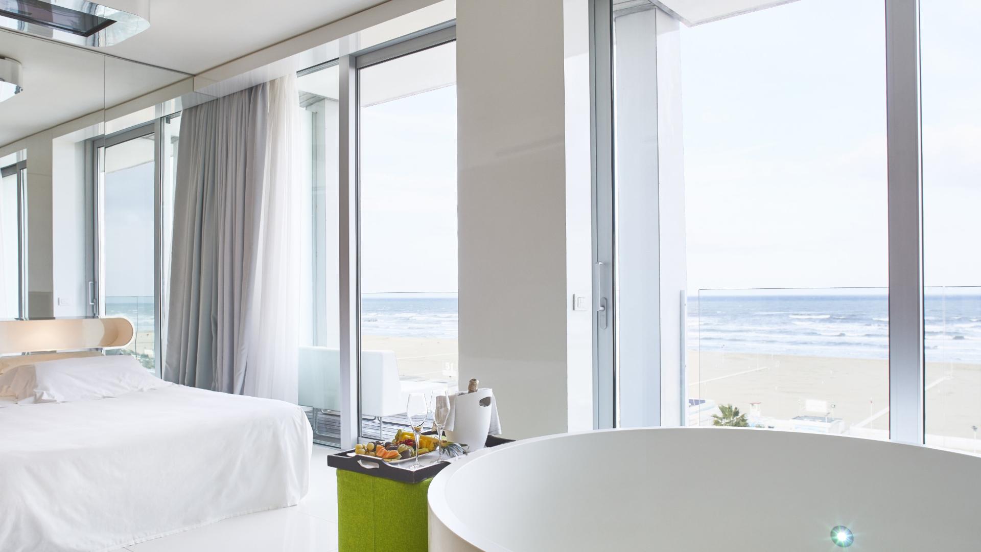 Camera moderna con vista mare, letto bianco e vasca rotonda.