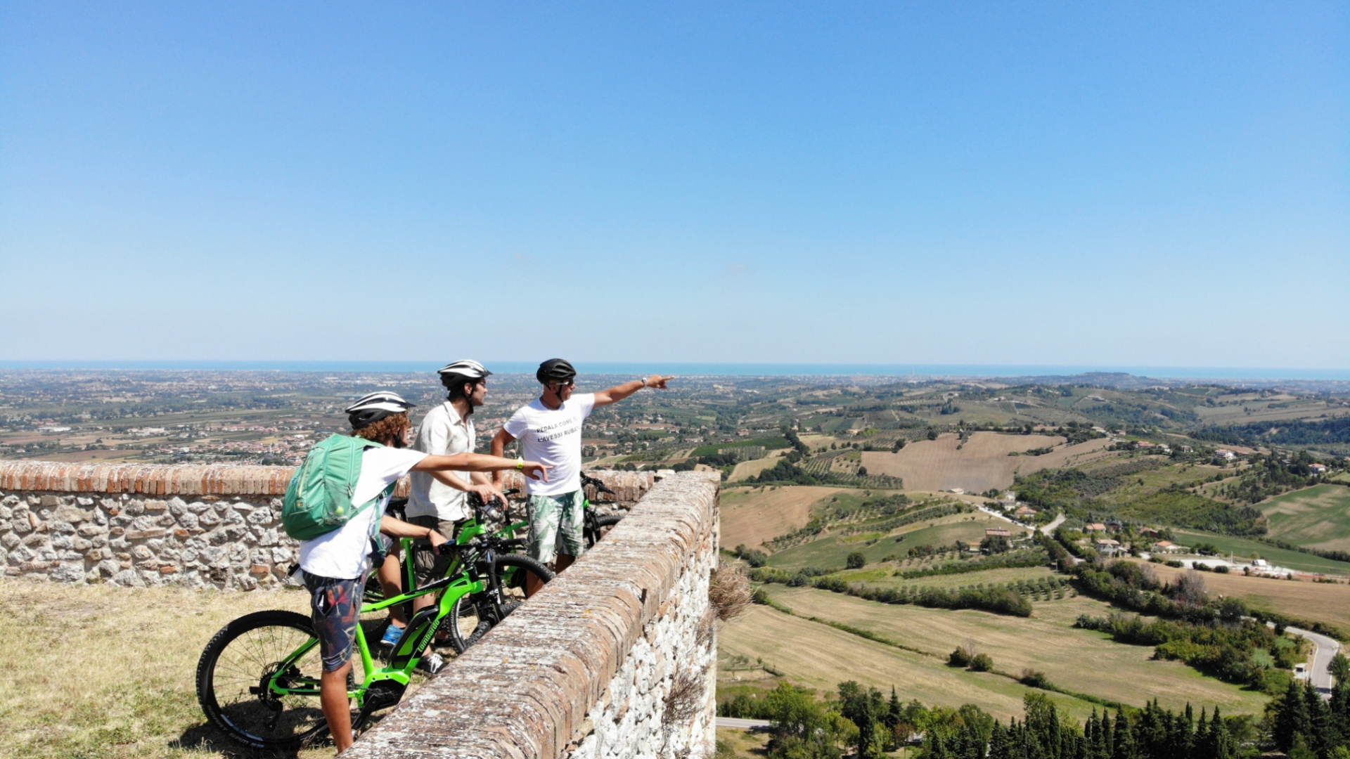 Ciclisti ammirano il panorama collinare dalla cima di un muro di pietra.