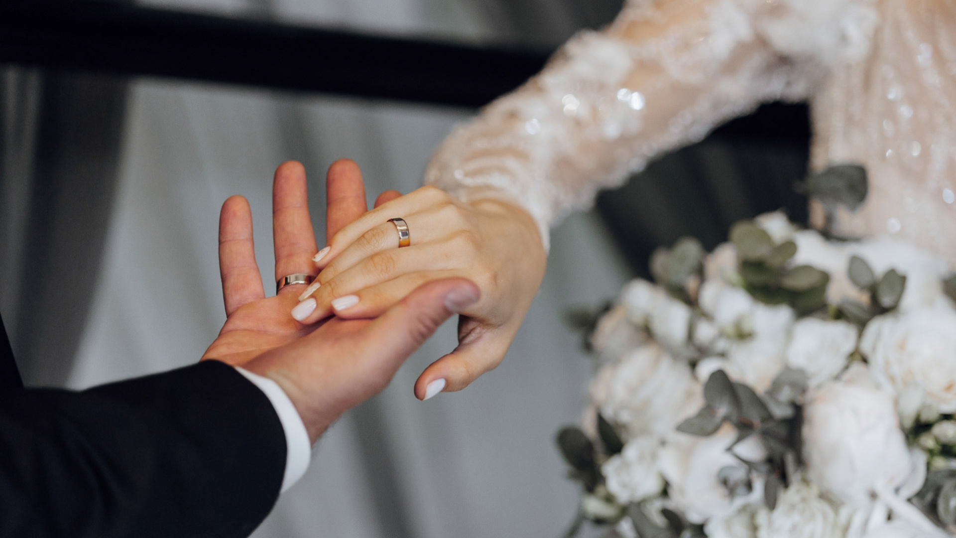 Scambio di anelli tra sposi, mani intrecciate e bouquet di fiori bianchi.