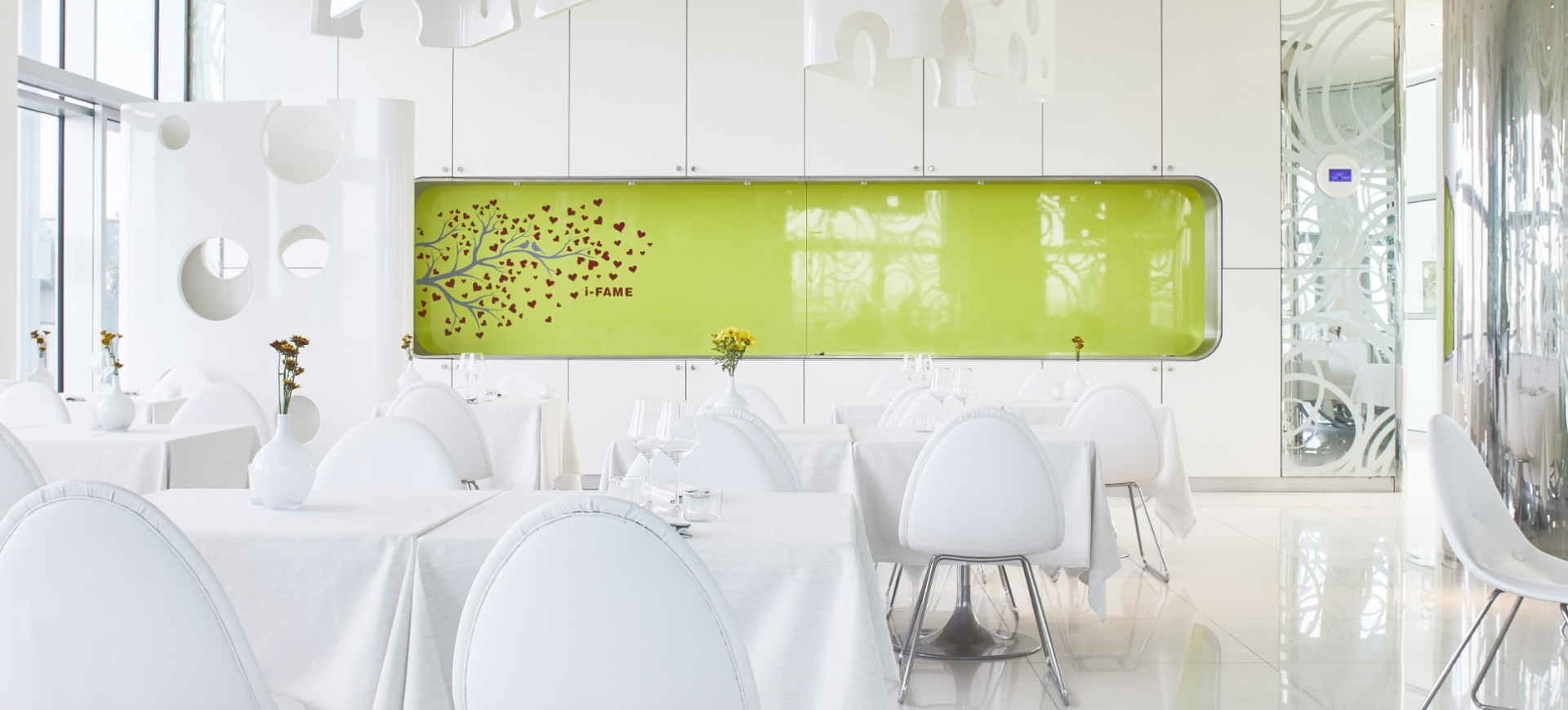 Moderno ristorante con arredamento bianco e verde, tavoli eleganti e decorazioni minimaliste.