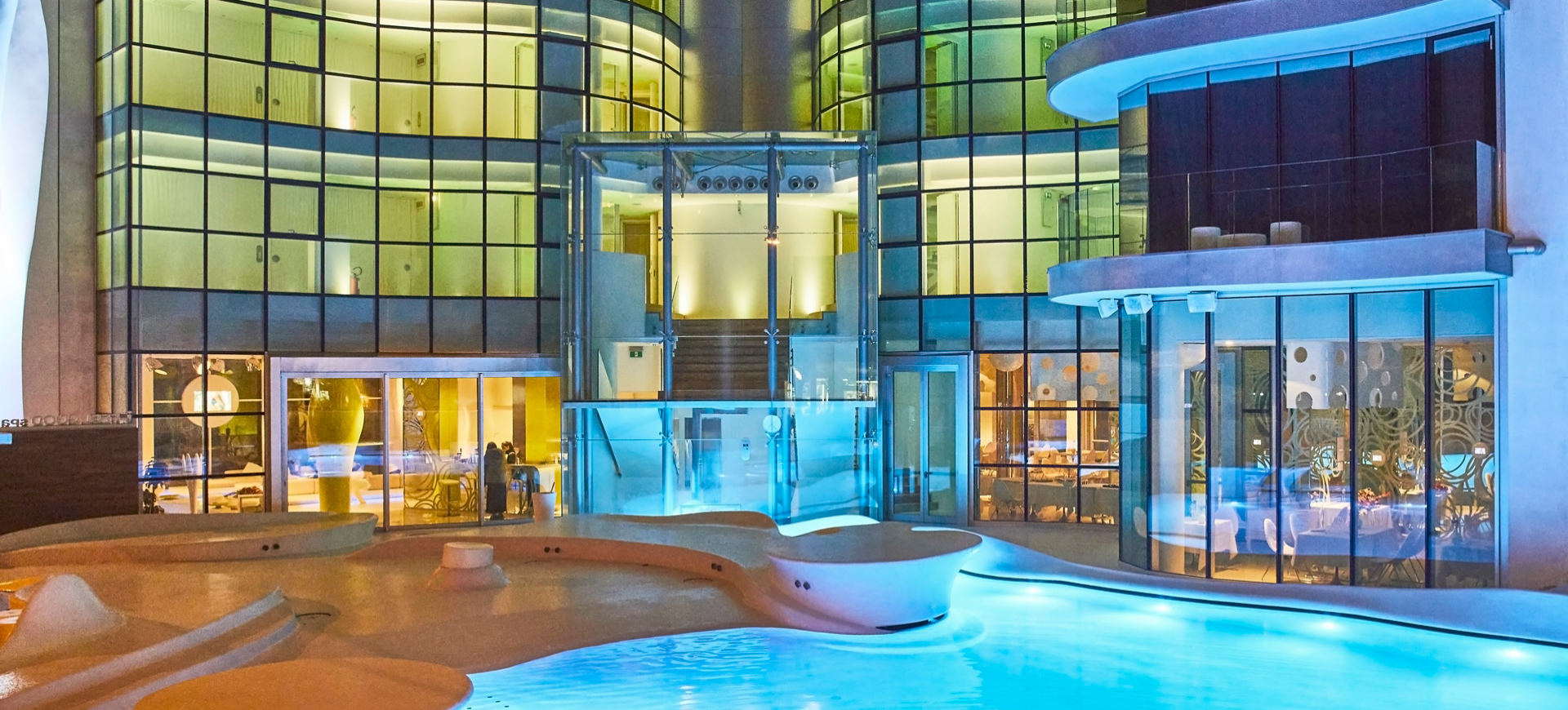Edificio moderno con piscina illuminata, vetrate curve e interni eleganti.