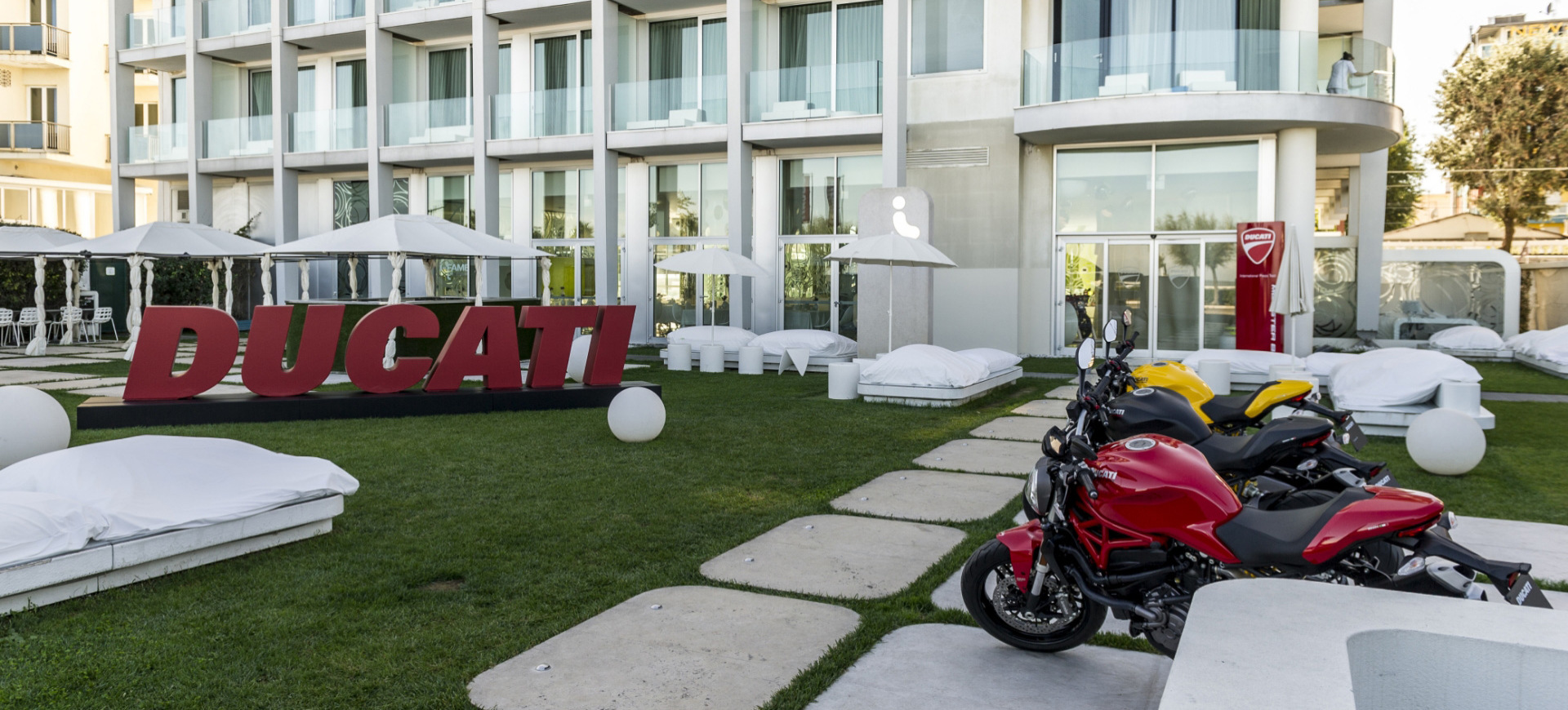 Moto Ducati parcheggiate davanti a un hotel moderno con insegna Ducati.