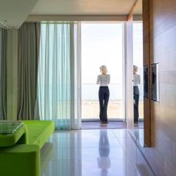 Woman gazes at the sea from a bright, elegant apartment, evoking peace and serenity.