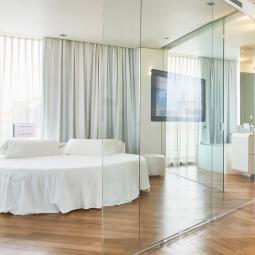 Camera moderna con pareti in vetro, letto rotondo e pavimento in legno.