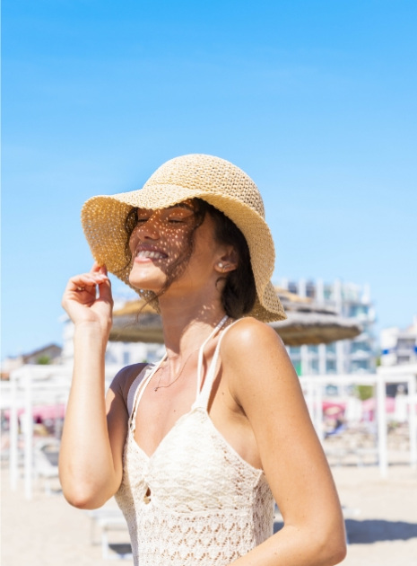 Donna sorridente con cappello di paglia in spiaggia sotto il sole estivo.