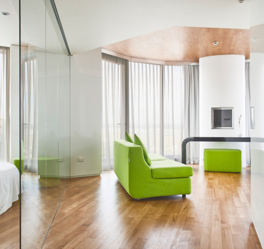 Moderno soggiorno con divano verde, pavimento in legno e ampie finestre.
