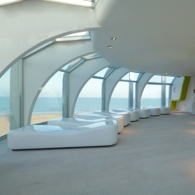 Interno moderno con vista sul mare, arredi bianchi e dettagli verdi.
