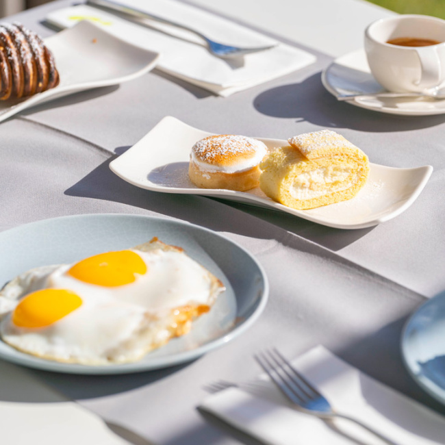 Colazione con uova al tegamino, dolci e tè su tavolo apparecchiato.