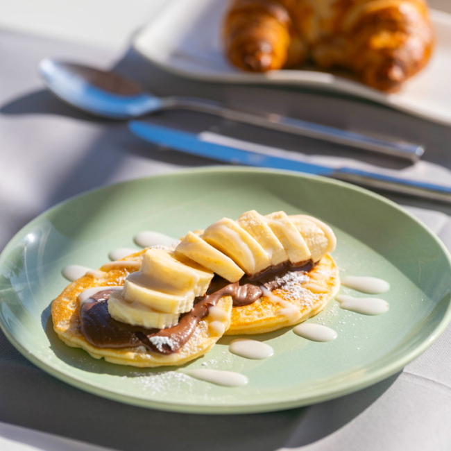 Pancake con banana e crema al cioccolato, accompagnato da un croissant.