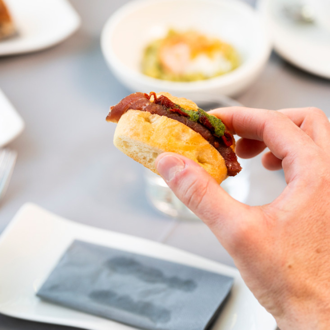 Mano tiene un panino gourmet con carne e salsa verde su un tavolo elegante.