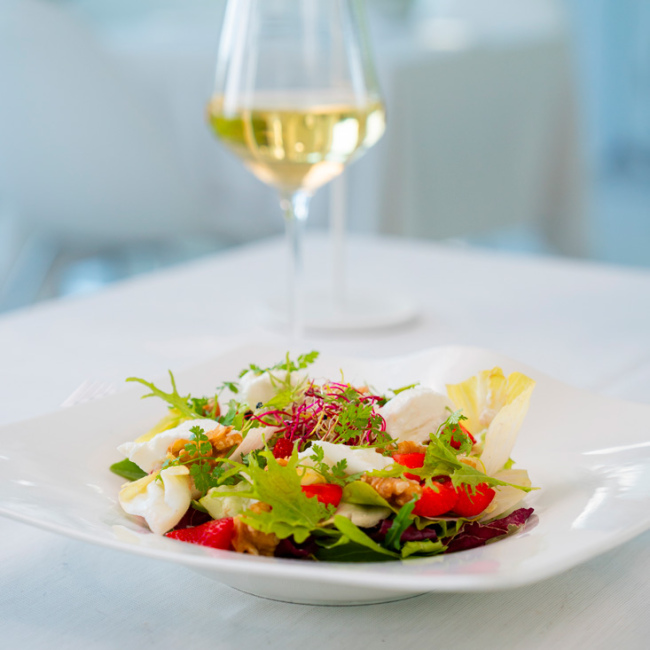 Bunter Salat mit frischem Grün und Weißweinglas in eleganter Umgebung.