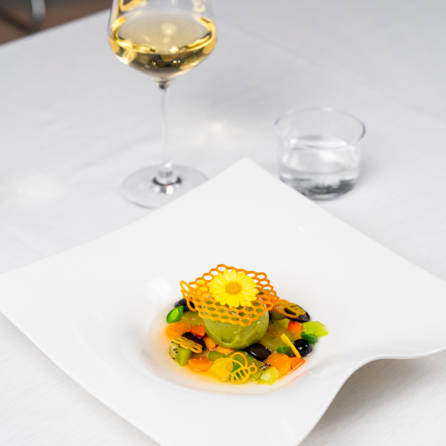 Elegantes Gericht mit Blumendekoration, lebhaften Farben und einem Glas Weißwein.
