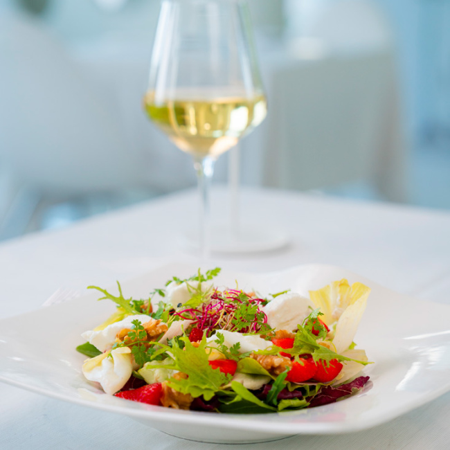 Insalata fresca con formaggio e noci, accompagnata da un bicchiere di vino bianco.