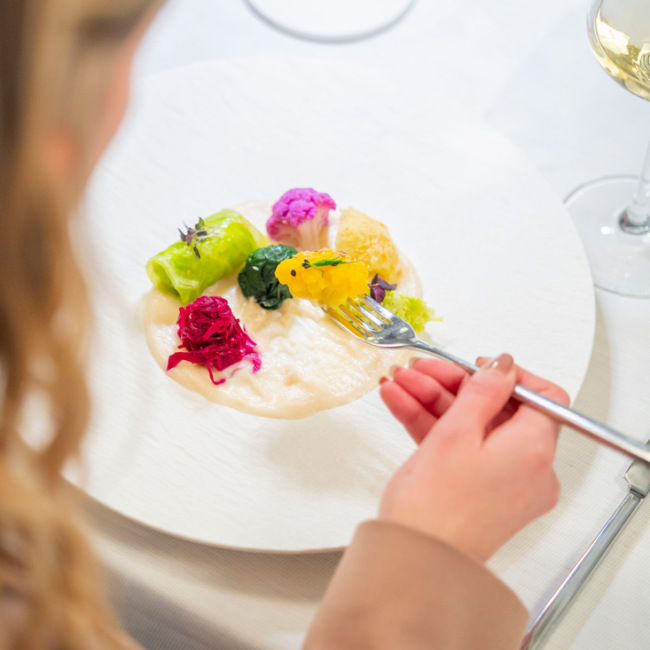 Piatto gourmet con verdure colorate e vino bianco in un ambiente elegante.