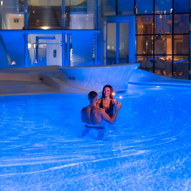 Coppia in piscina illuminata, atmosfera romantica con candela.