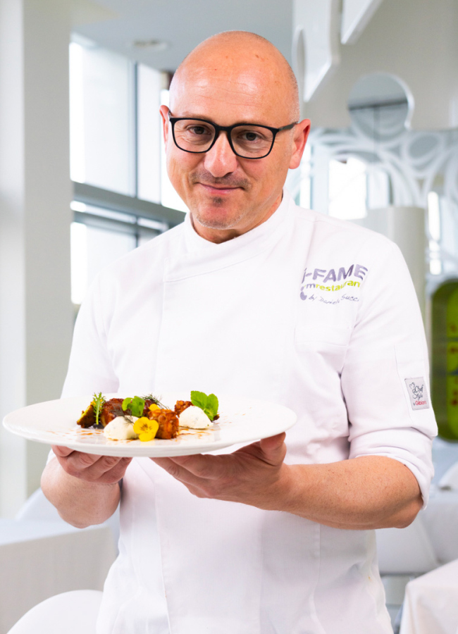 Lächelnder Koch präsentiert ein elegantes Gericht in einem hellen Restaurant.