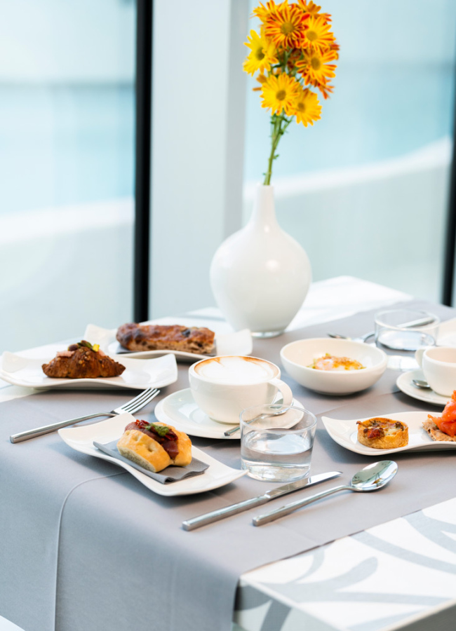 Tavola da colazione elegante con caffè, dolci, fiori gialli e piatti raffinati.