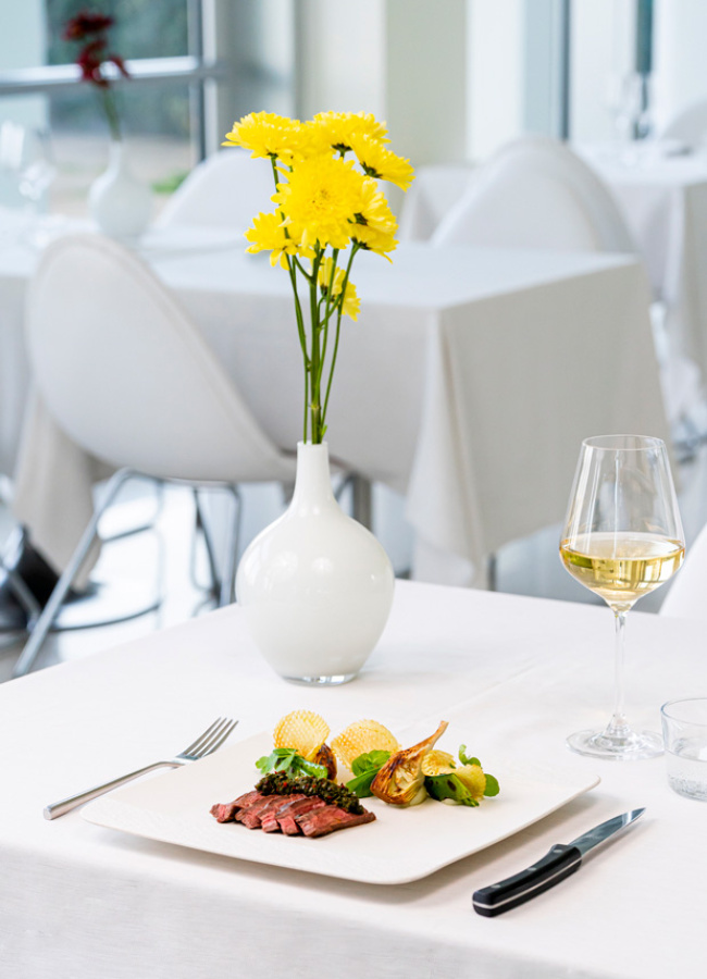 Eleganter Tisch mit Gourmetgericht und Wein, gelbe Blumen schmücken die raffinierte Atmosphäre.