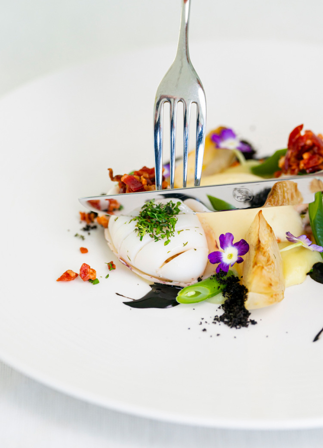Piatto gourmet con presentazione elegante, fiori edibili e vari ingredienti raffinati.