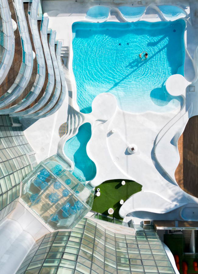 Vista dall'alto di una piscina moderna con design curvilineo e terrazza vetrata.