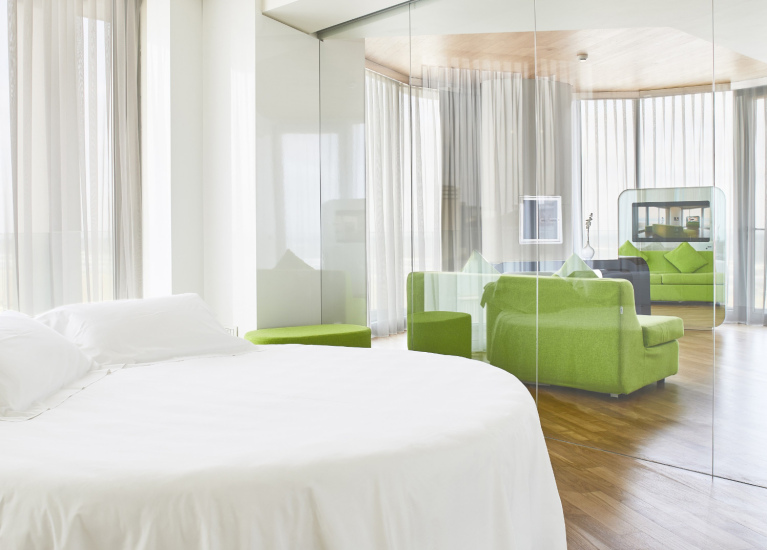 Camera moderna con letto bianco, divano verde e pareti di vetro.